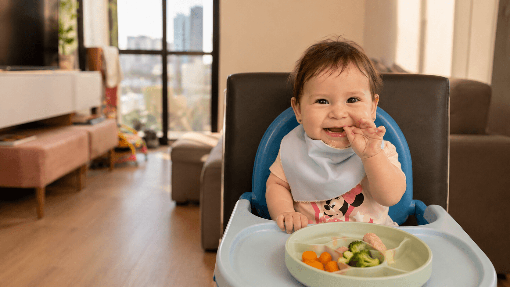 Bebê sorrindo na cadeira de alimentação, com um prato de legumes à frente